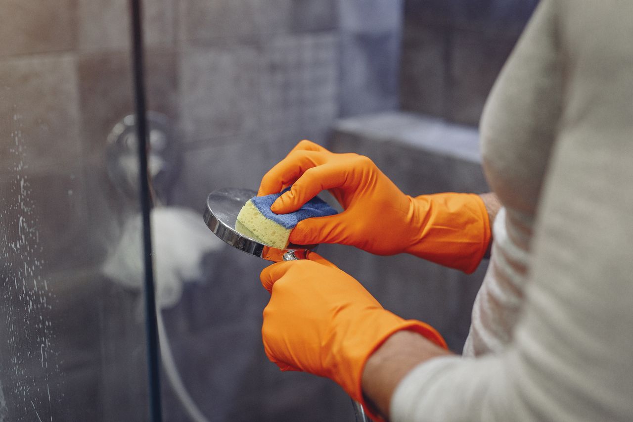 services-08 Crop faceless male in orange rubber gloves wiping by sponge shower nozzle