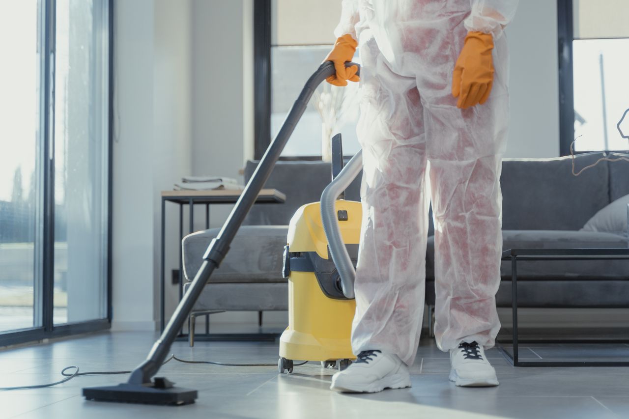services-03 A cleaner in protective coveralls and gloves vacuuming a contemporary living room.